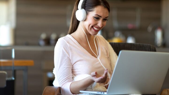 A Woman Wearing white Head Phones Working on Her Laptop